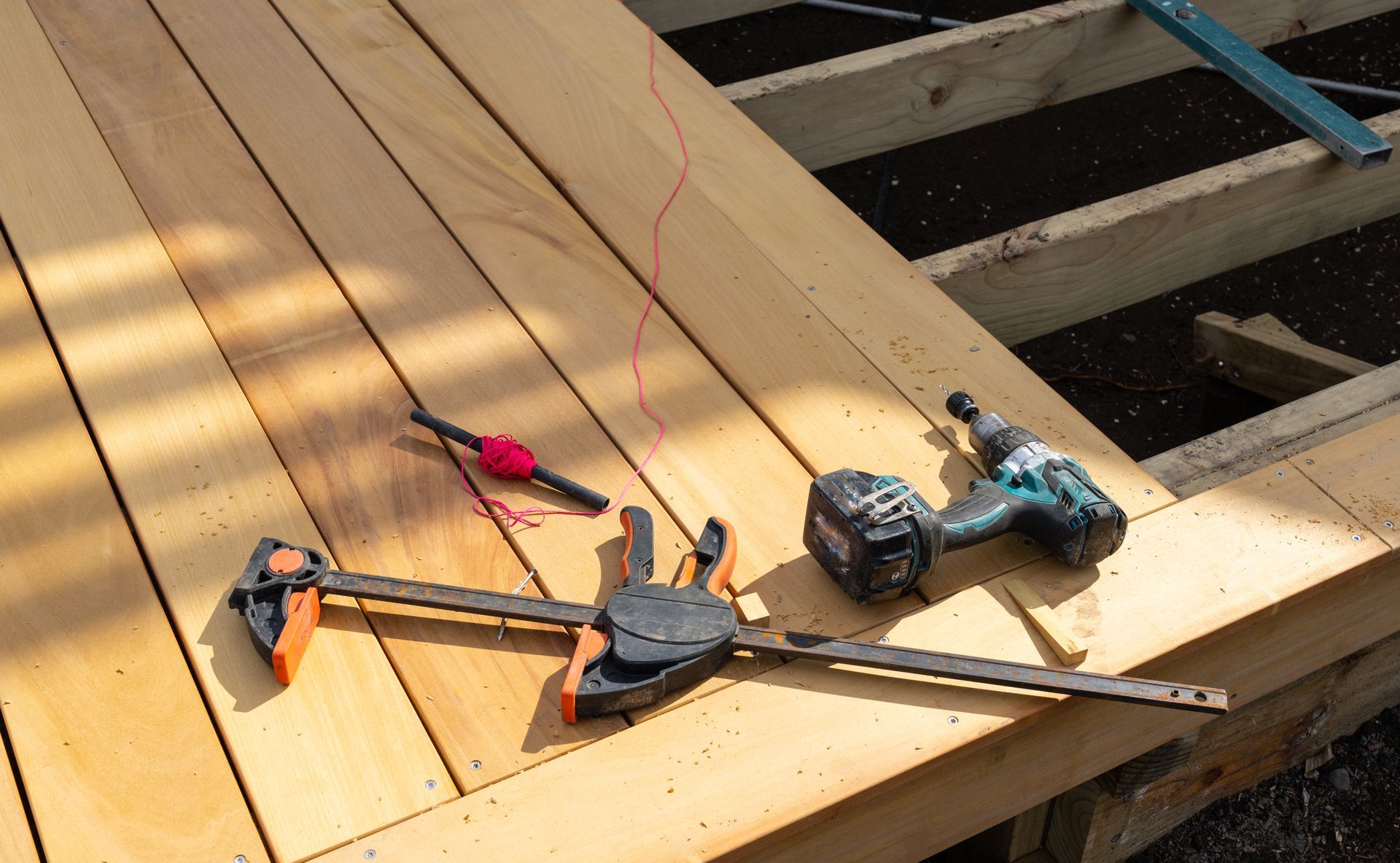 A drill and a bar clamp resting on freshly installed wooden deck boards during construction. A drill and a bar clamp resting on freshly installed wooden deck boards during construction.