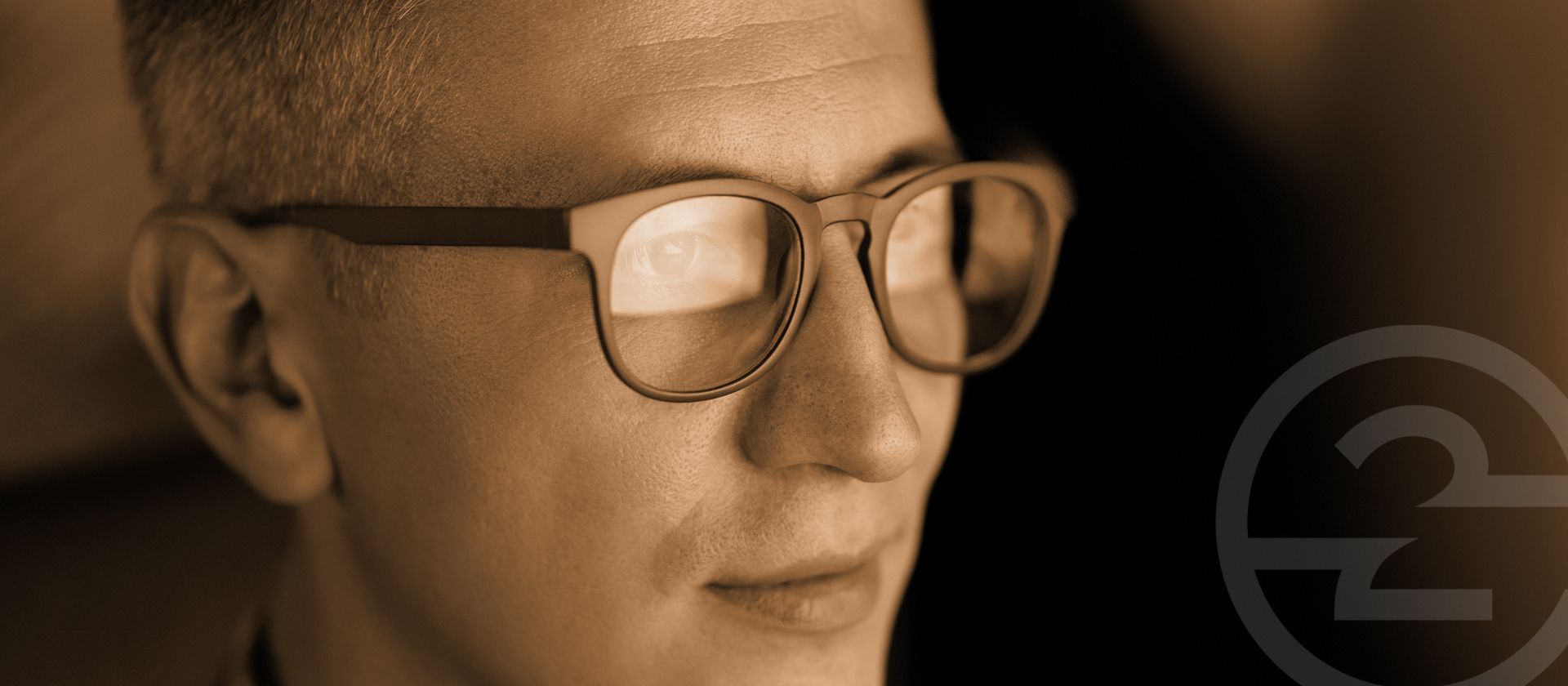Close-up of a man in glasses looking downward in warm sepia light