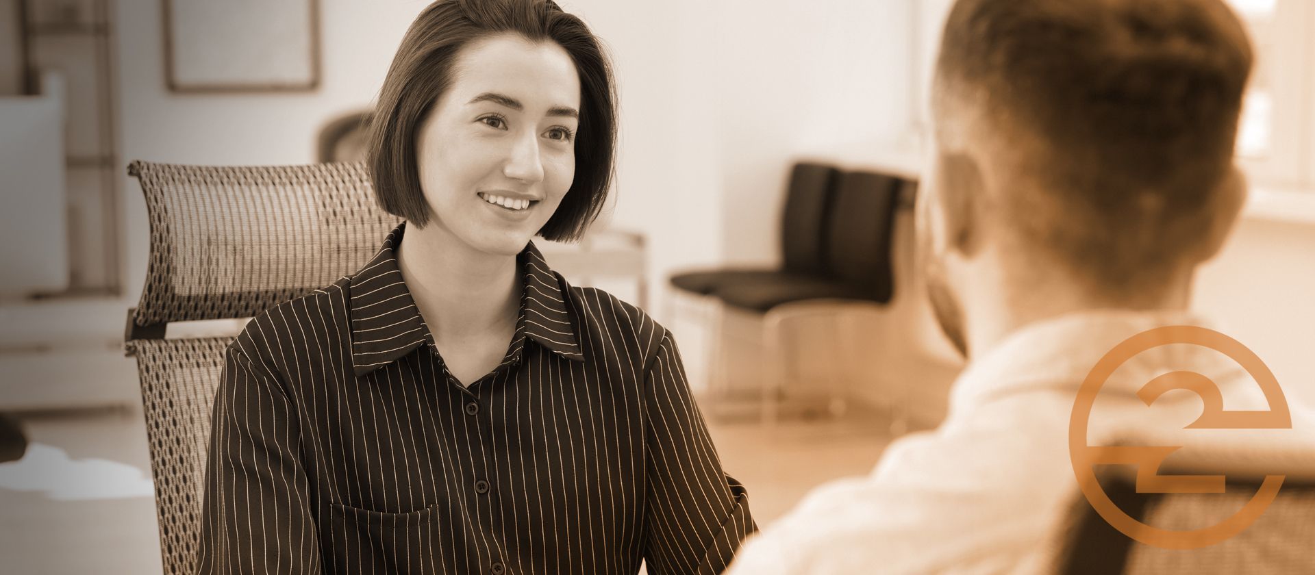 Two people talking across a table in a warm, softly lit office setting