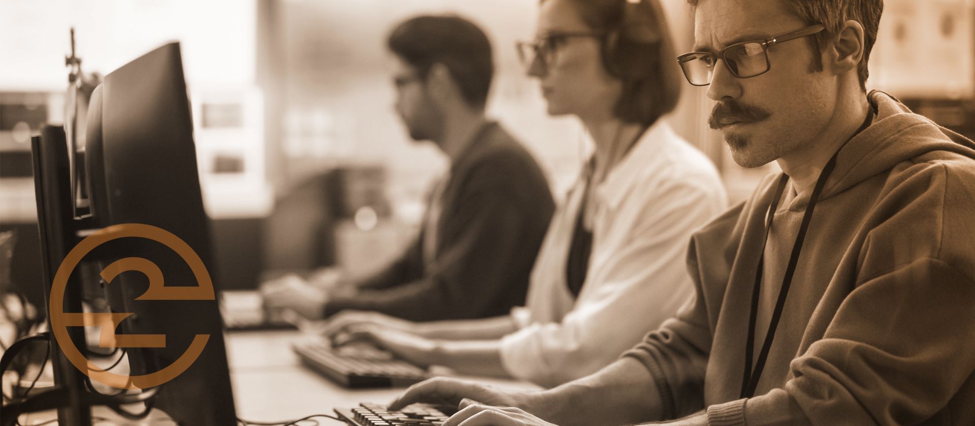 People working on computers in a lab setting. One person wears glasses and a mustache. Sepia tone.