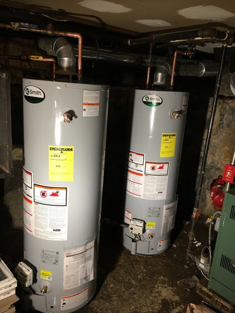 Two water heaters are sitting next to each other in a basement.