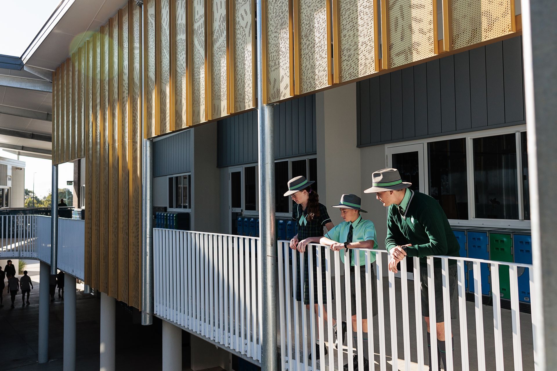 Three Students in Green Uniforms Lean on a White Railing on a School Balcony — BOLD Architecture + Interior Design In Mackay, QLD