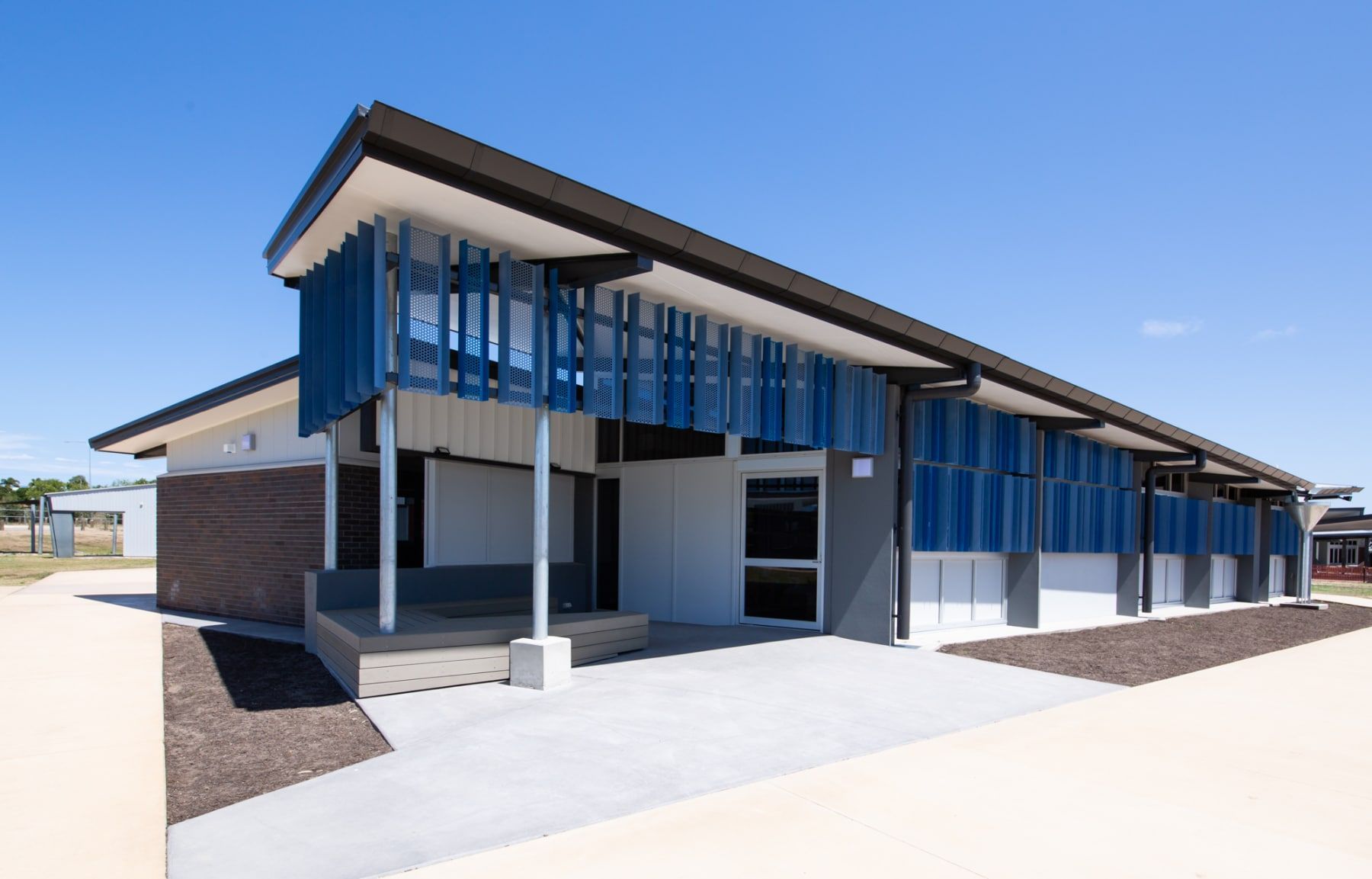Modern Single-story Building With Blue Accents on a Sunny Day. Features a Dark Roof, and Concrete and Gravel Landscaping — BOLD Architecture + Interior Design In Mackay, QLD