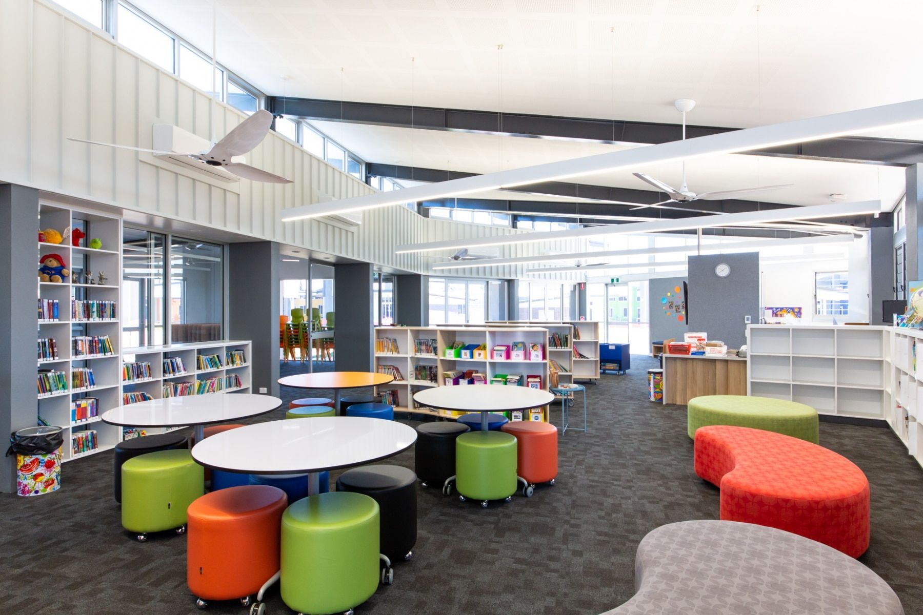 A Modern School Library With White Tables, Colorful Ottomans, Bookshelves, and Large Windows — BOLD Architecture + Interior Design In Mackay, QLD