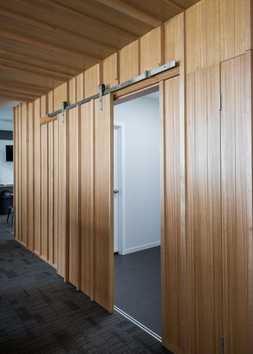 Wooden Barn Door, Open to a White Room. Light Wood Paneling, Grey Carpet, Ceiling Panels — BOLD Architecture + Interior Design In Mackay, QLD