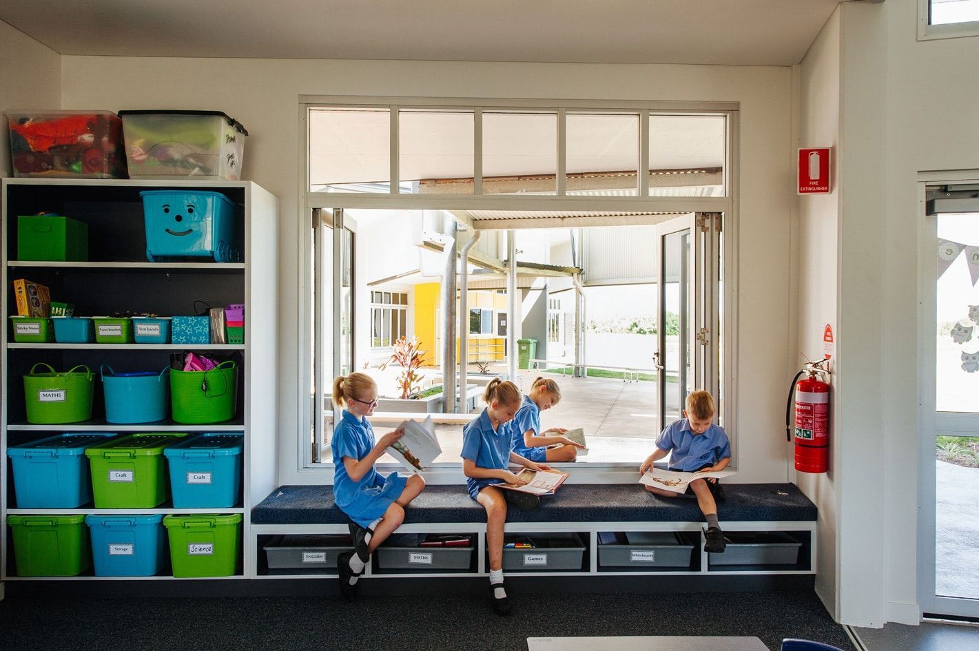 Children Reading on a Window Seat Inside a Classroom, With Shelves of Supplies Visible — BOLD Architecture + Interior Design In Mackay, QLD