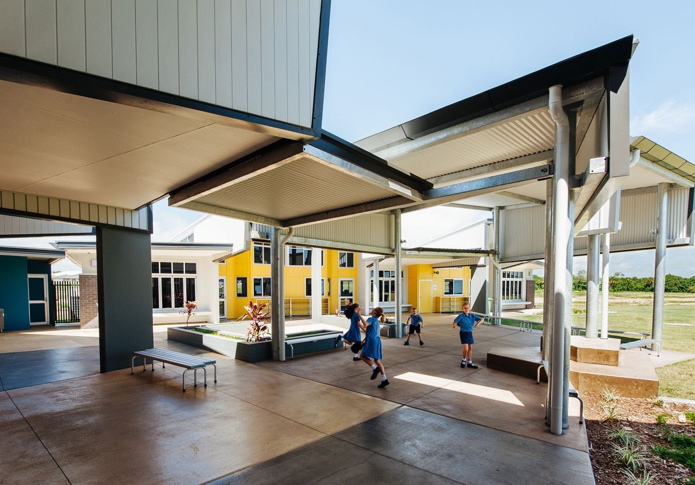 Children Playing in a School Courtyard Under a Shaded Walkway. Yellow and Blue Buildings in the Background — BOLD Architecture + Interior Design In Mackay, QLD