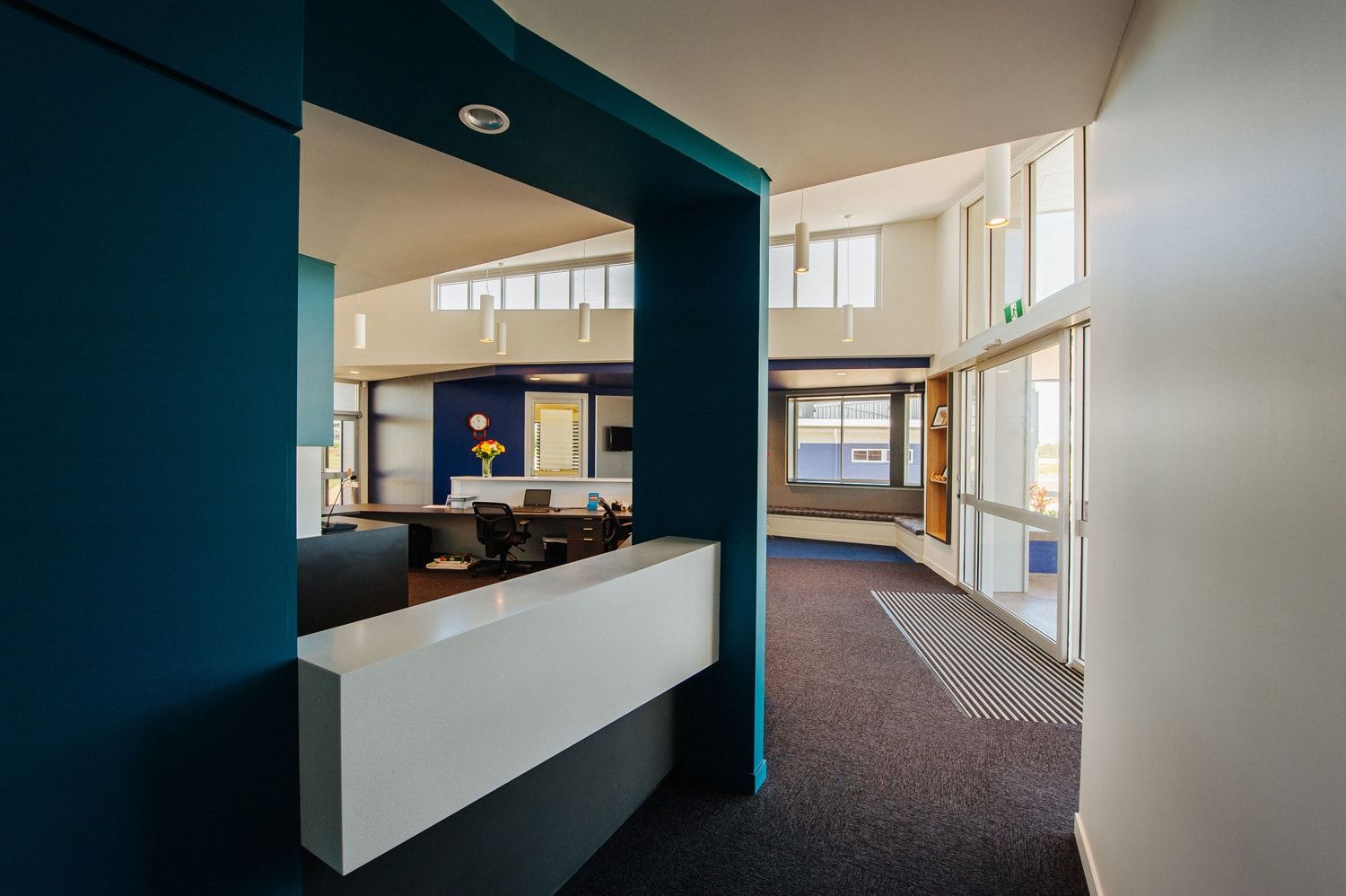 Reception Desk With White Counter and Blue Wall, Leading to a Bright Hallway — BOLD Architecture + Interior Design In Mackay, QLD