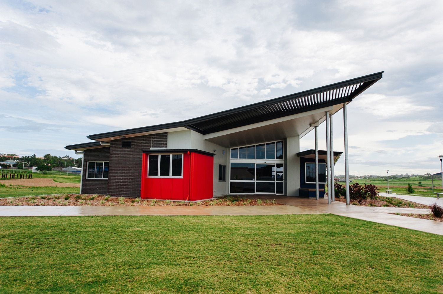 Modern Single-story Building With Red, Brown, and White Exterior, Angled Roof, Glass Windows, and Green Lawn — BOLD Architecture + Interior Design In Mackay, QLD