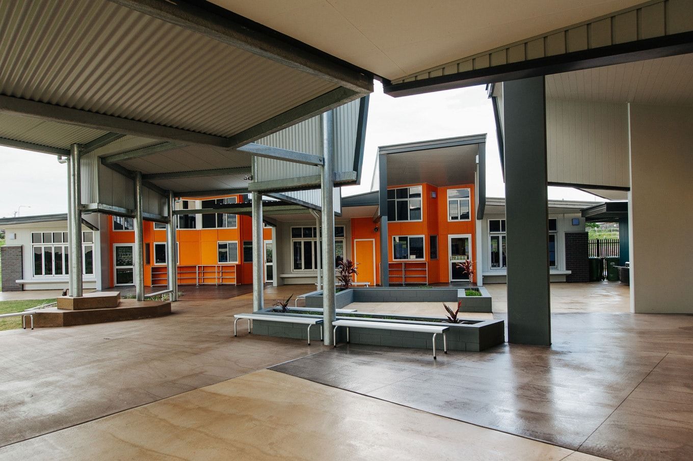 Outdoor Courtyard With Orange and White Buildings Under a Shaded Walkway, With Grey Seating — BOLD Architecture + Interior Design In Mackay, QLD