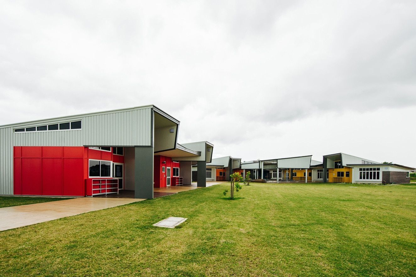 Modern School Buildings With Red and Yellow Accents, on a Grassy Field Under a Cloudy Sky — BOLD Architecture + Interior Design In Mackay, QLD