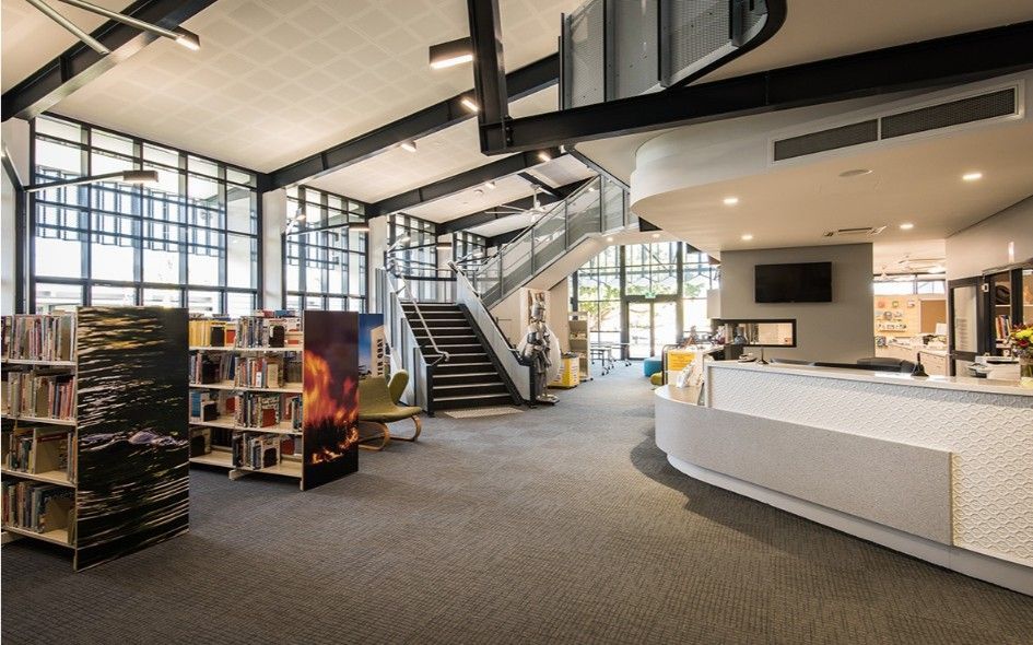 Library Interior With Bookshelves, a Staircase, and a Reception Desk Under a High Ceiling — BOLD Architecture + Interior Design In Mackay, QLD