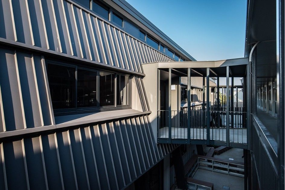 Exterior of Modern Building With Dark Gray Metal Siding and a Pedestrian Bridge — BOLD Architecture + Interior Design In Mackay, QLD