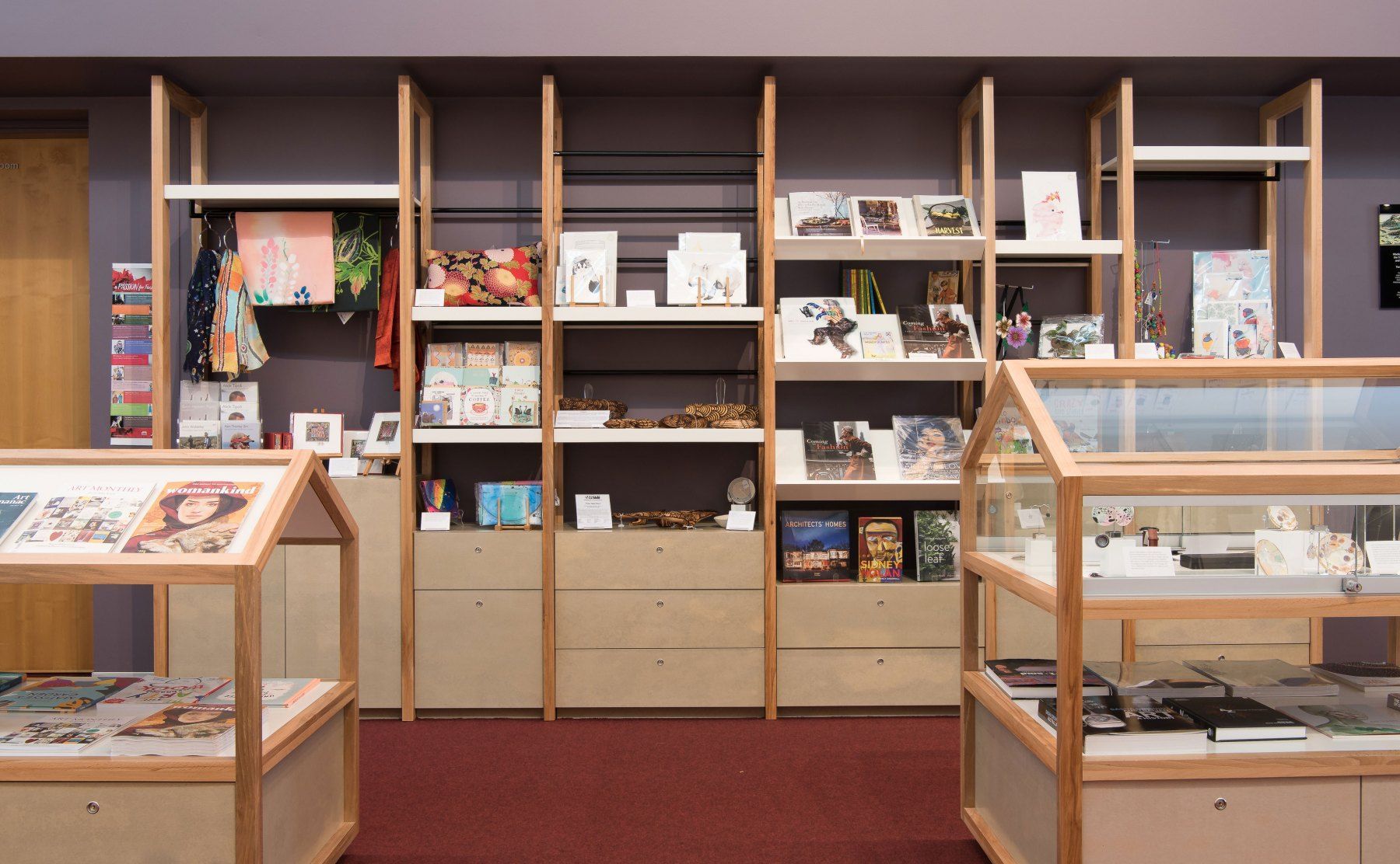A Small Shop Interior With Light Wood Shelves and Display Cases Against a Maroon Wall — BOLD Architecture + Interior Design In Mackay, QLD