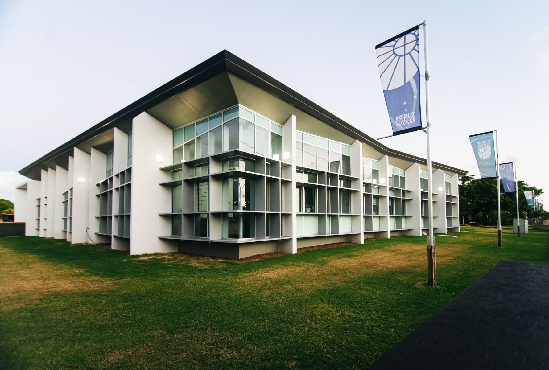 Modern White Building with Glass Windows, Flags Line the Lawn — BOLD Architecture + Interior Design In Mackay, QLD