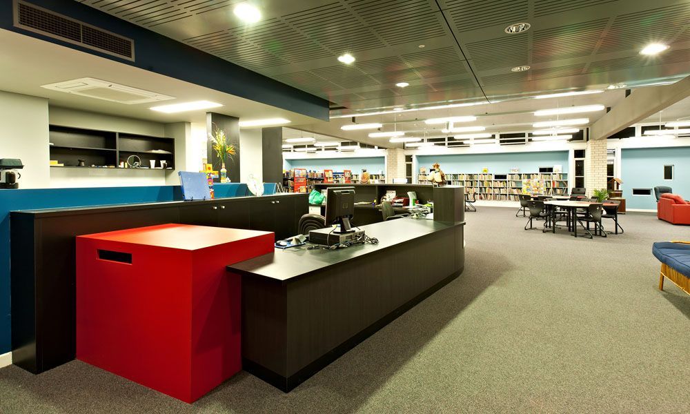 Interior of a Modern Library With a Red Block, Dark Desk, and Rows of Books — BOLD Architecture + Interior Design In Mackay, QLD