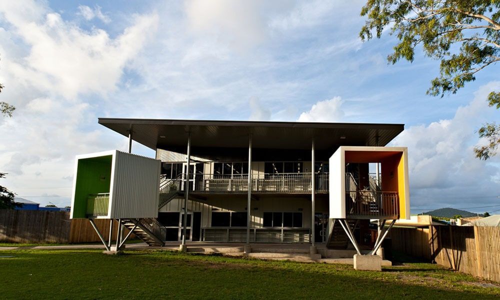 Two-story Building With Box-like Rooms in Green and Orange, Supported by Metal Legs, on a Green Lawn — BOLD Architecture + Interior Design In Mackay, QLD