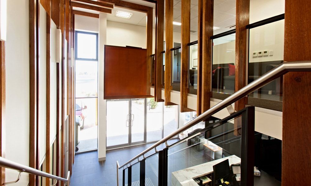 Staircase With Wood Paneling, Glass Walls, and Stainless Steel Handrails Leading Down From an Entryway — BOLD Architecture + Interior Design In Mackay, QLD