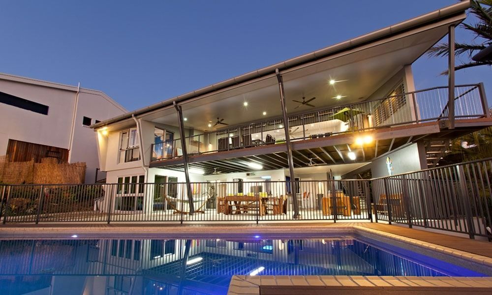 Two-Story Modern House with A Pool at Dusk; a Deck, Lights, and Fence Are Visible — BOLD Architecture + Interior Design In Mackay, QLD