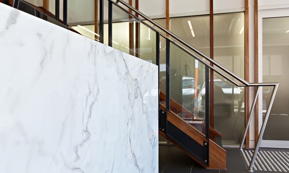 Marble-faced Wall Next to Staircase With Glass and Metal Railing. Wooden Steps, Natural Light — BOLD Architecture + Interior Design In Mackay, QLD