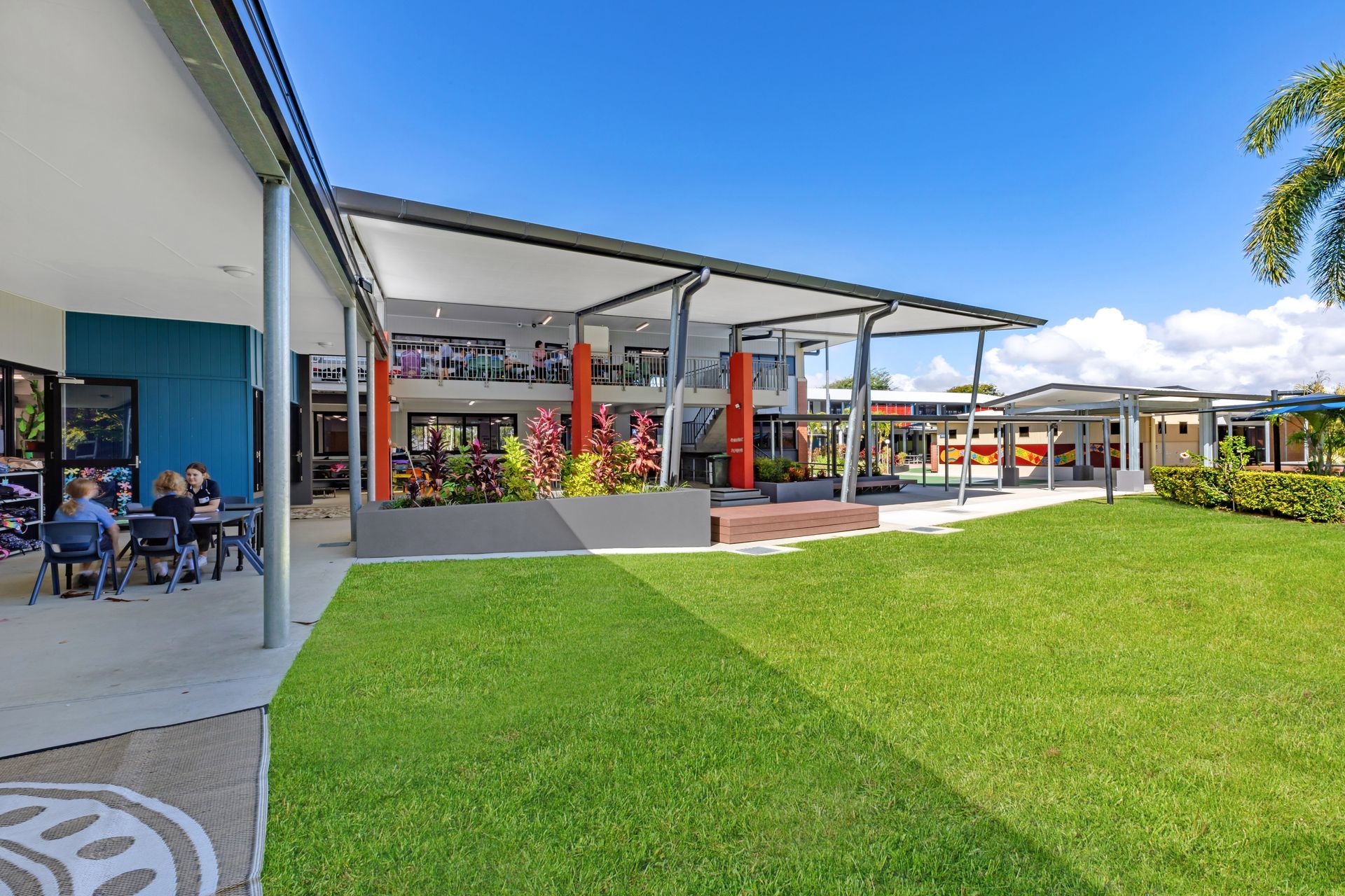 Exterior School Building With Green Lawn, Covered Walkways, and Students at Tables — BOLD Architecture + Interior Design In Mackay, QLD