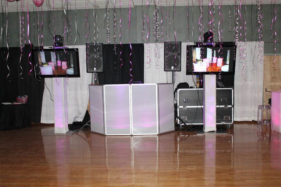DJ setup with monitors and speakers. Pink and silver streamers hang from ceiling. White and black backdrop.