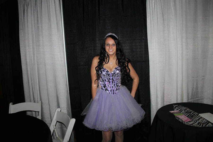 Woman in a lavender dress and tiara posing in front of white and black curtains.