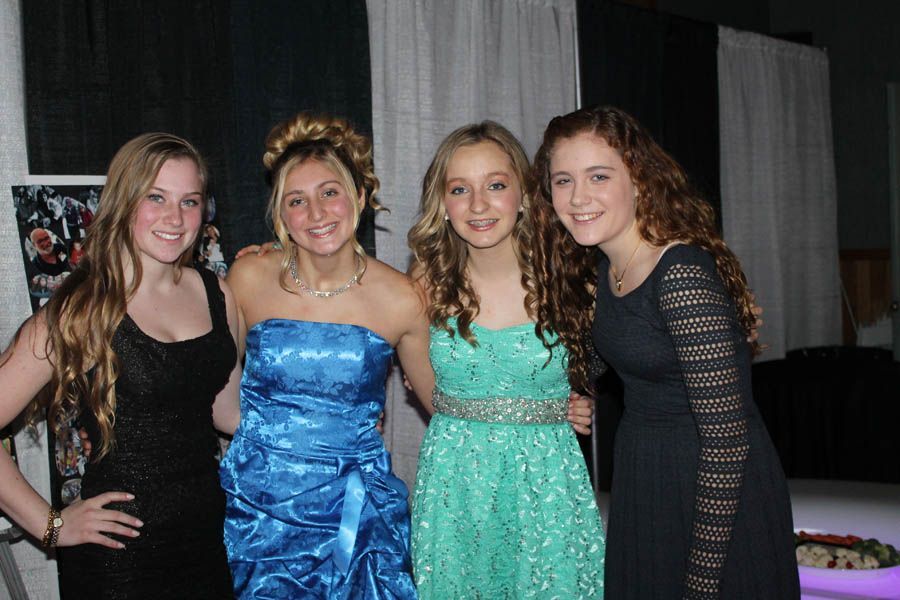 Four girls in prom dresses, smiling and posing indoors.