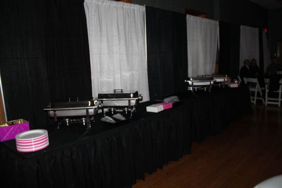 Buffet with black table skirts and silver chafing dishes under white curtains.