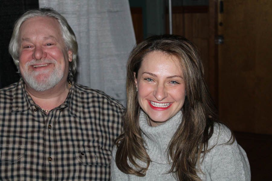 Man with a white beard and woman with long brown hair smiling indoors.