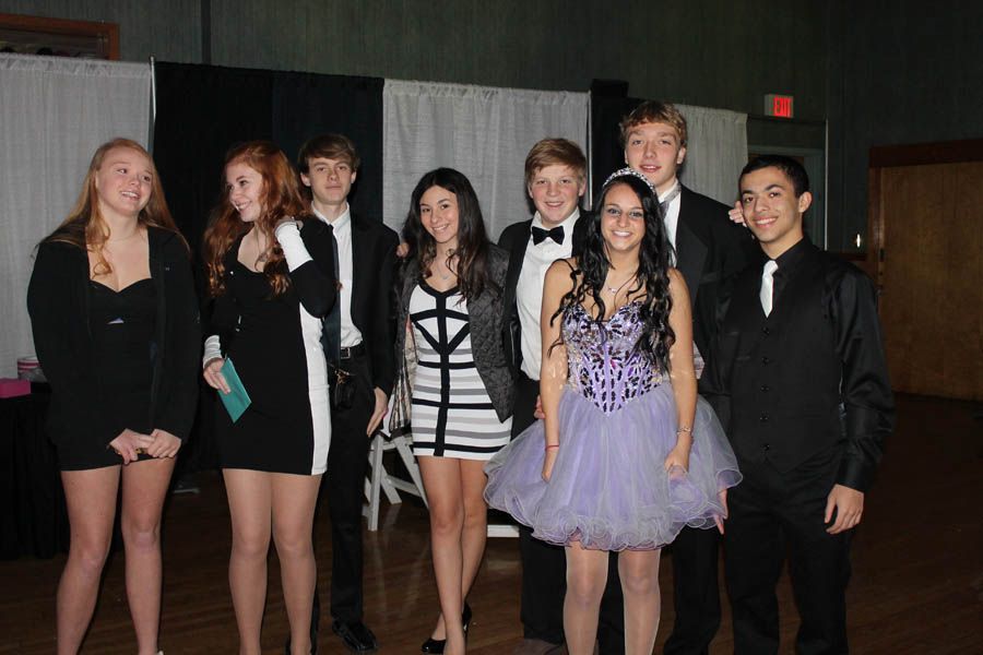 Group of eight people dressed in formal attire, smiling, indoors.