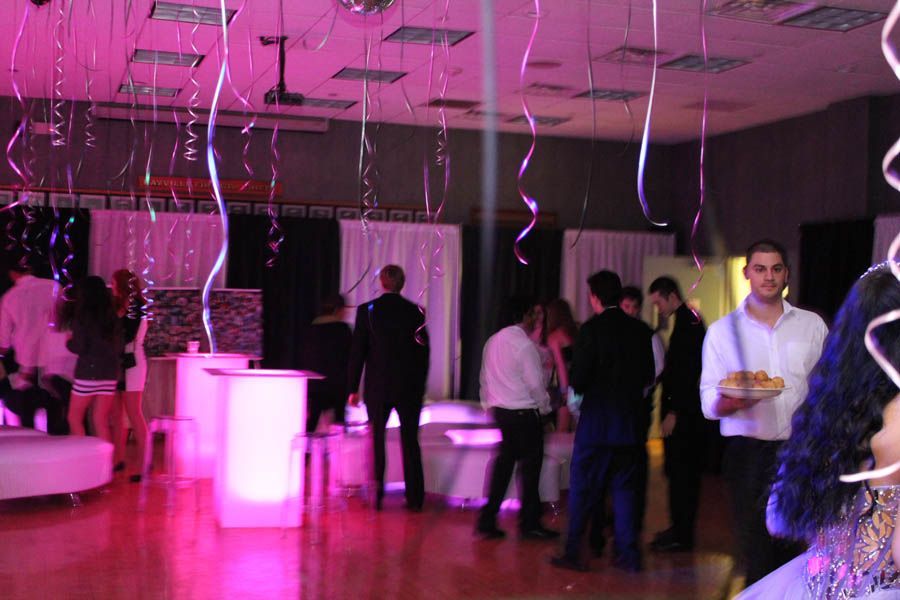 People at a party, pink lighting, streamers, and white tables.