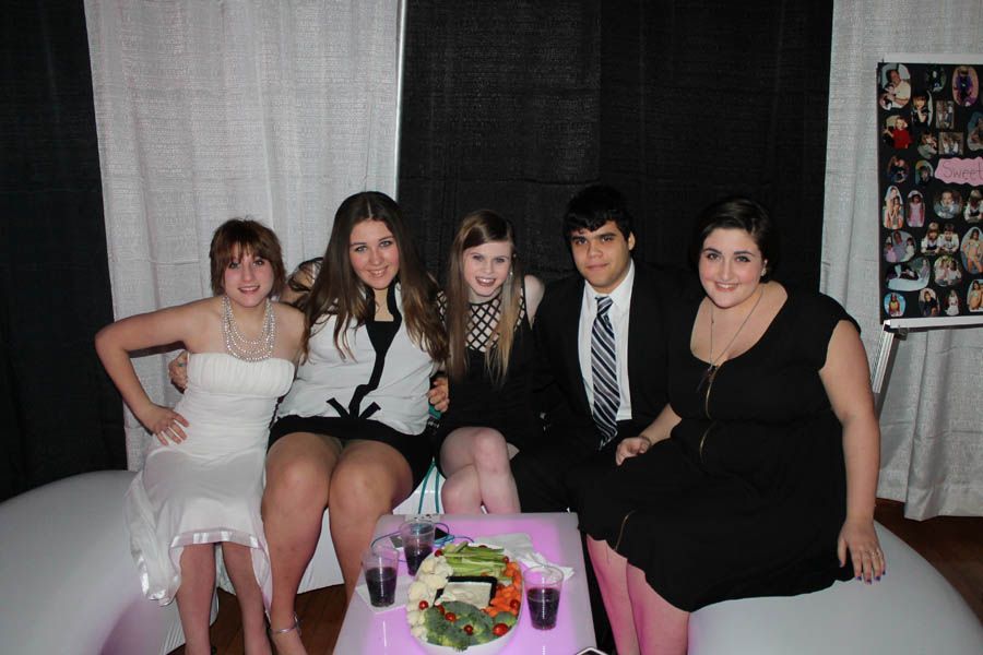 Five people seated on a white sofa at an event, with food and drinks on the table.
