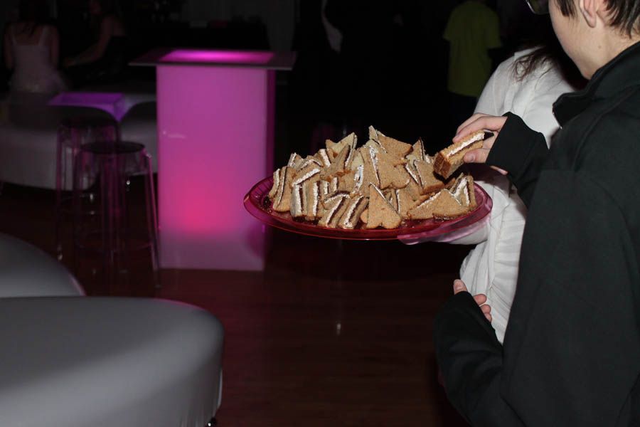 Person holding a plate of triangle-cut sandwiches at an event with pink lit furniture.