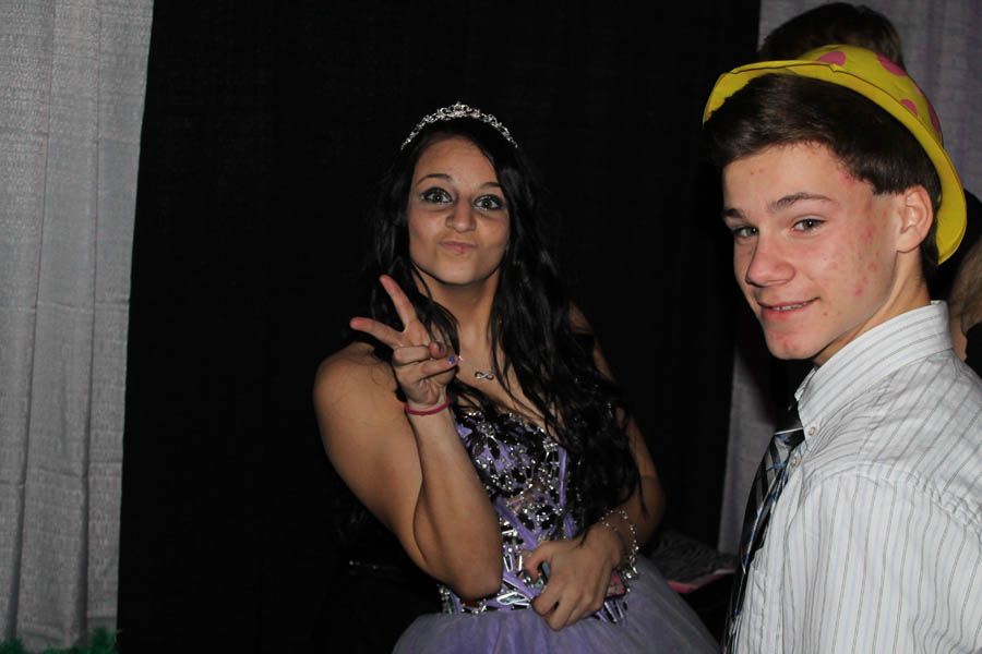 Woman in formal dress with tiara and peace sign next to a man wearing a cowboy hat and striped shirt.