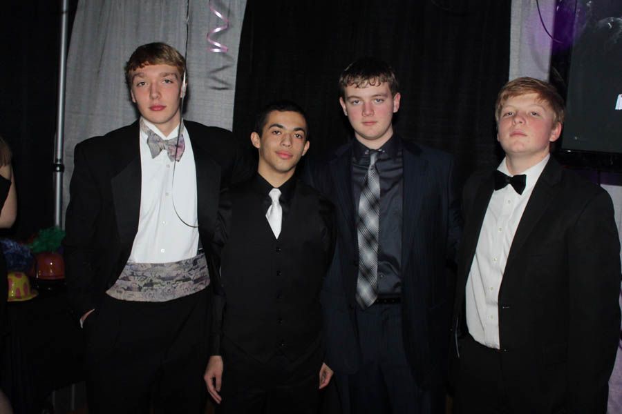 Four young men in formal attire posing for a photo at an event. They are in tuxedos, smiling slightly.