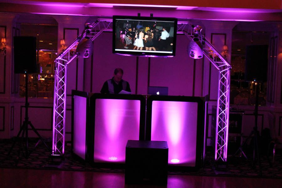 DJ setup with purple lighting and a screen displaying video footage.