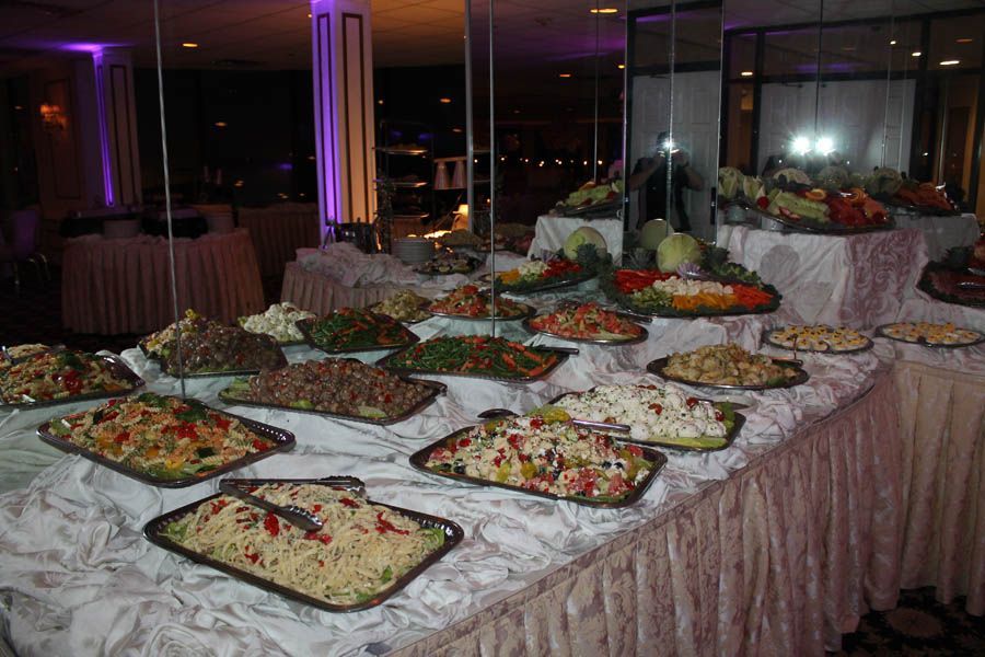 Buffet table with various salads in silver trays, white tablecloth, indoor setting.