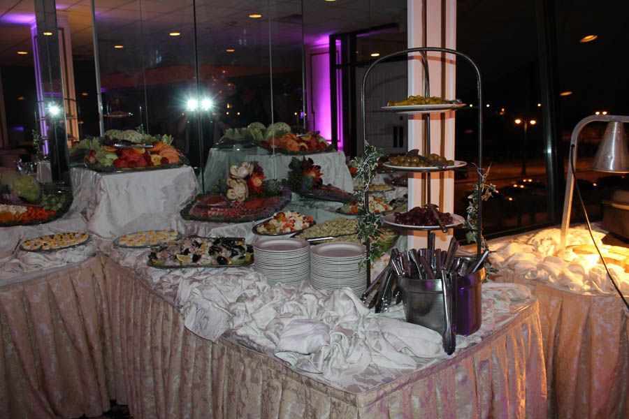 Buffet table with various food platters. Beige tablecloths, tiered serving stand, and evening setting.