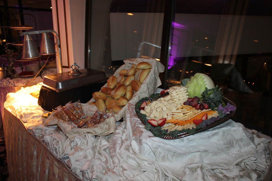 Buffet with rolls, salad, bread and hot food under warming lamps, set on a draped table near a window.
