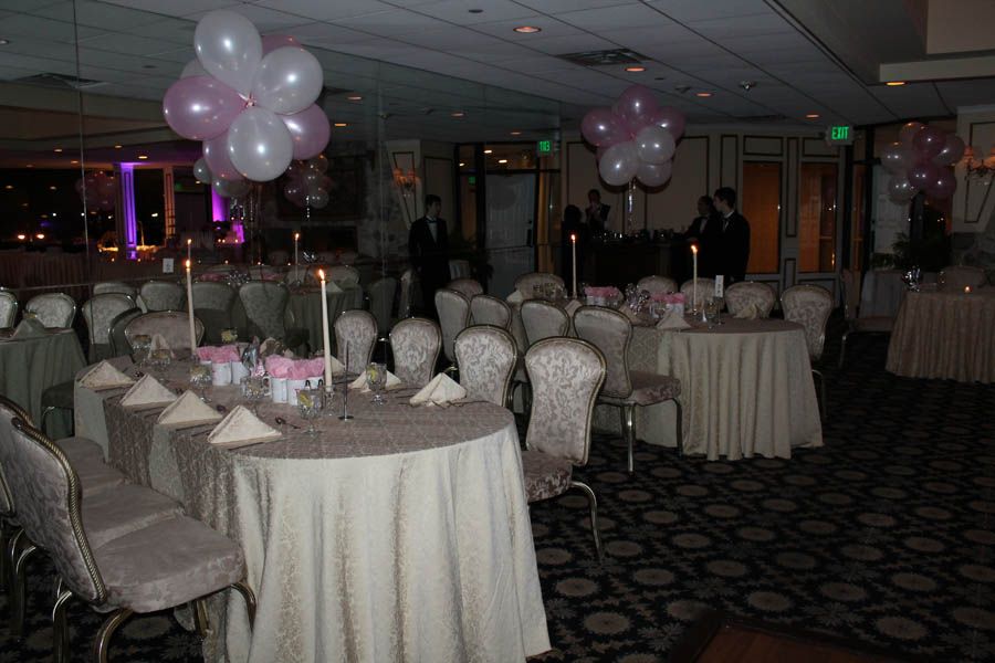 Event hall with round tables set for a party, decorated with balloons and candles.