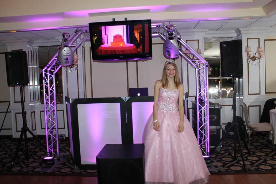 Teen girl in pink dress poses near a DJ setup at a formal event, lit with purple lights.