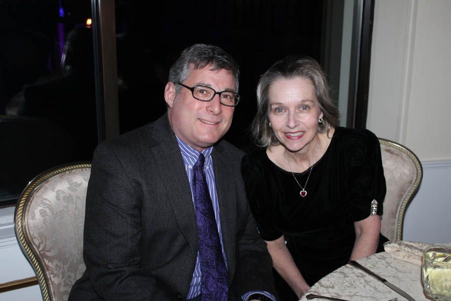 Man and woman seated at a table. Man in suit, woman in black dress. Smiling, indoor setting.