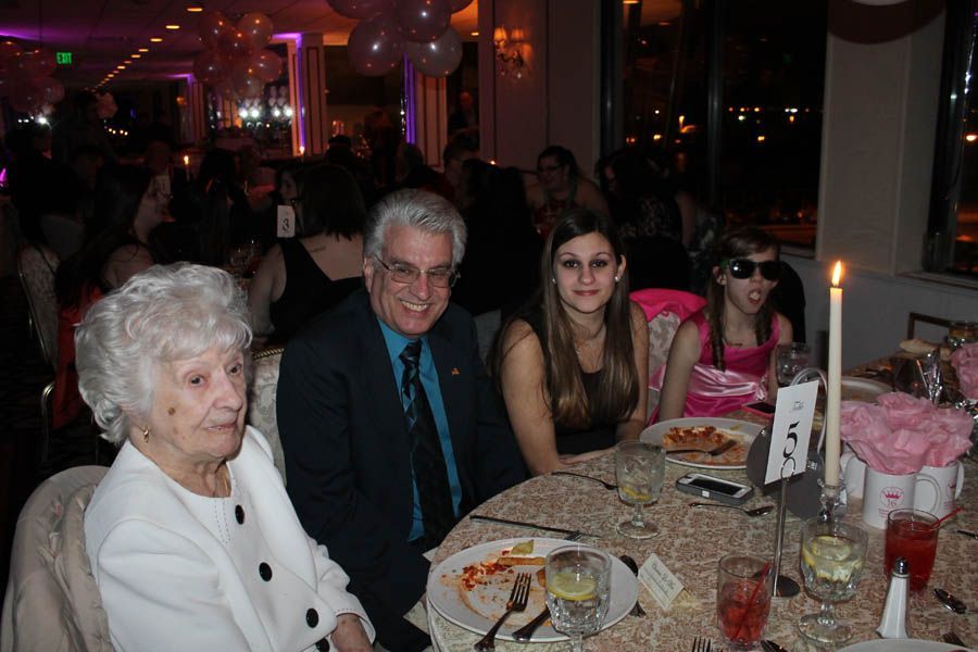 People at a formal dinner table, including an elderly woman, a man in a suit, and two young women