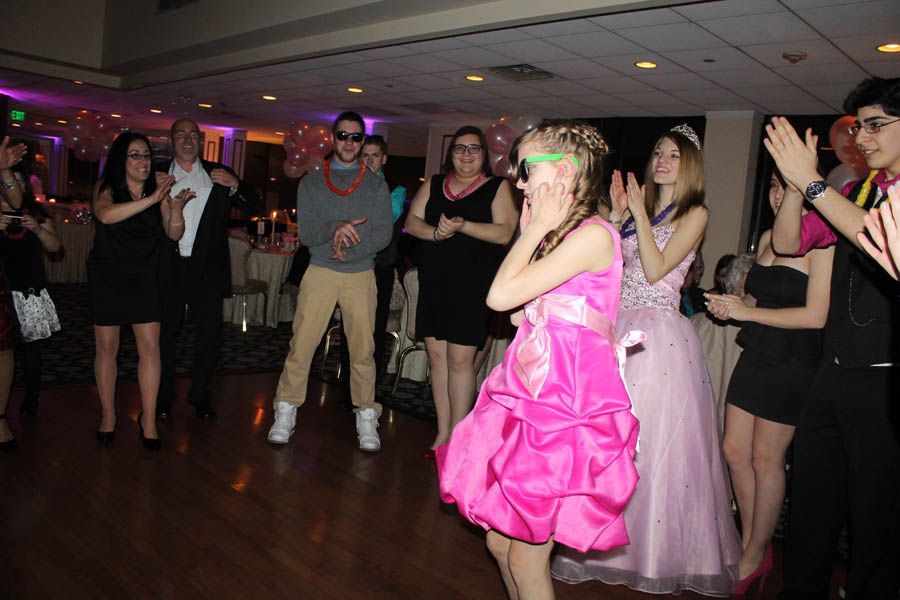 People clapping at a party, a girl in a pink dress is the center of attention, excited expression.