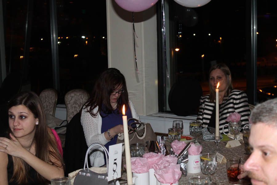 People seated at a table with candles, balloons, and city lights visible through a window.