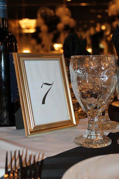 Gold framed table number 7 on white tablecloth with wine glass and bottle.
