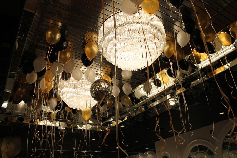 Ornate chandeliers with gold, black, and white balloons; decorative ceiling for a celebration.