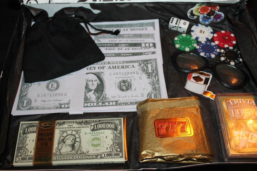 A box of prop money, poker chips, dice, sunglasses, a lighter, and chocolate bars wrapped like gold.