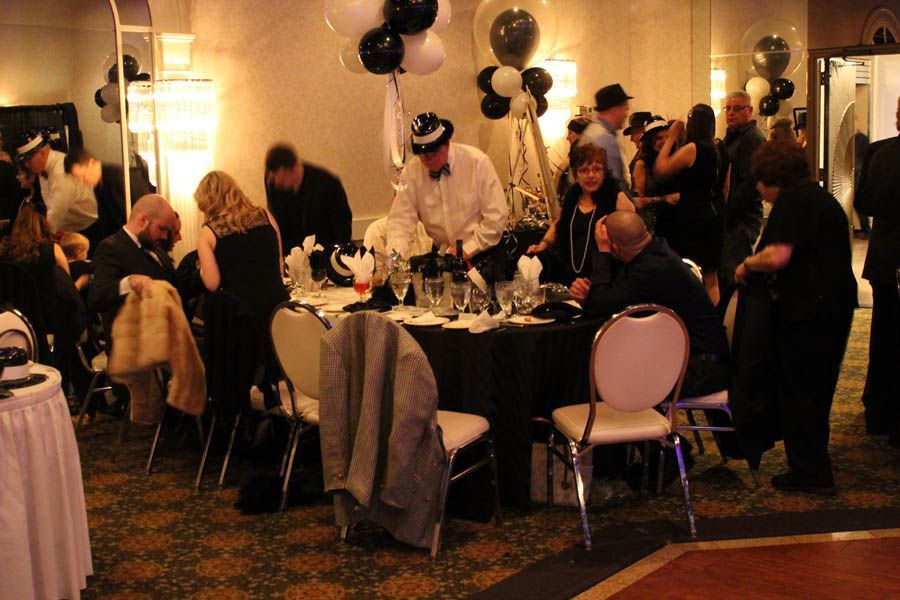 People at a party, dressed in black and white attire. Balloons and tables with decorations.